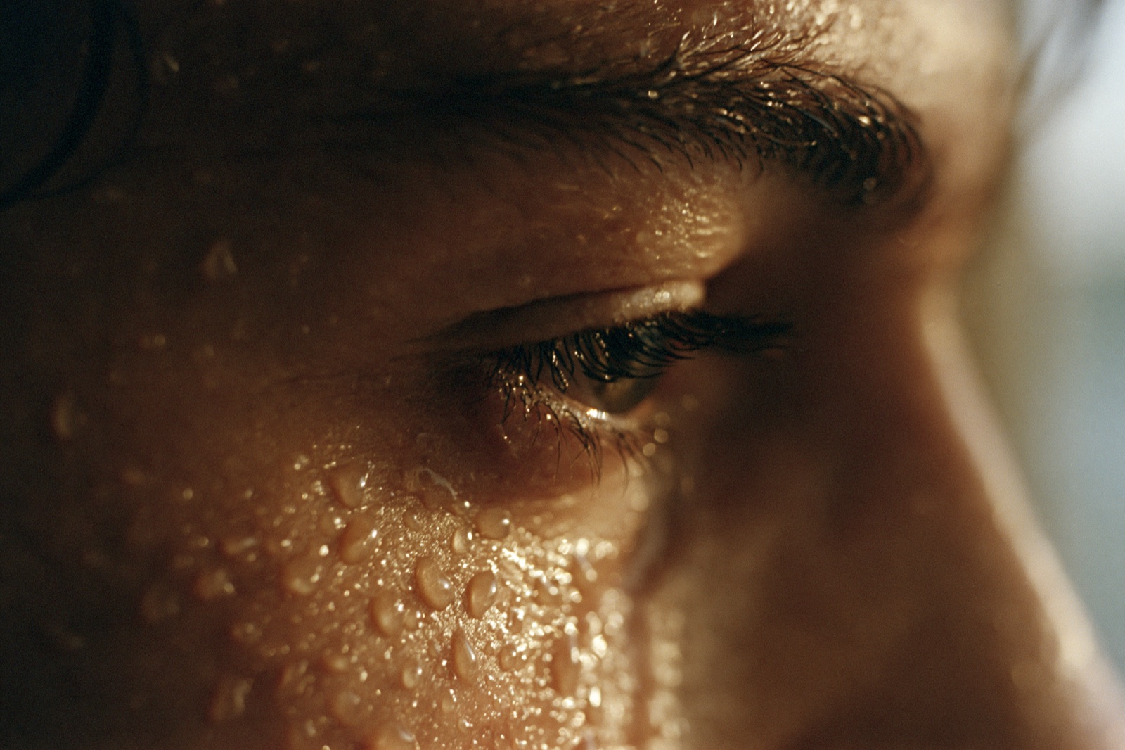 A close view of a face after hard effort, brow and cheek beaded with sweat in warm low light