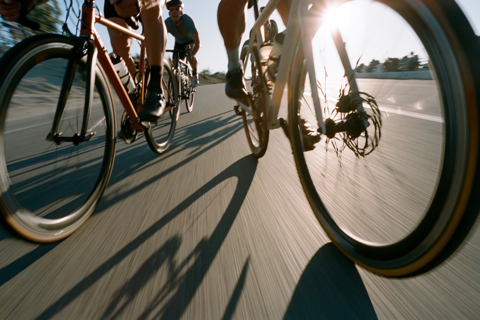 Road cyclists racing wheel to wheel into low sun, shot from the tarmac with motion blur